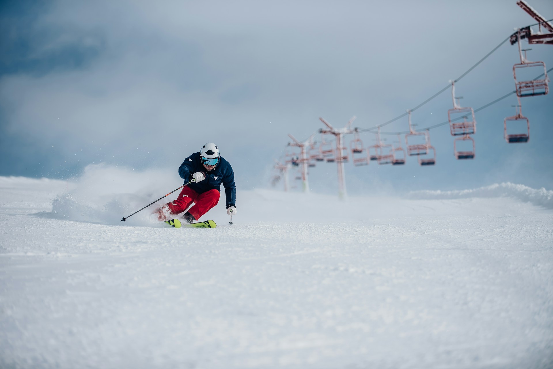 A person skiing down a piste with cable cars in the background