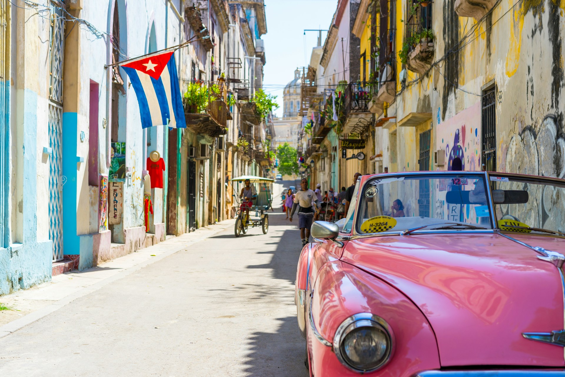 A lively street in Cuba with a bright red classic car in the foreground